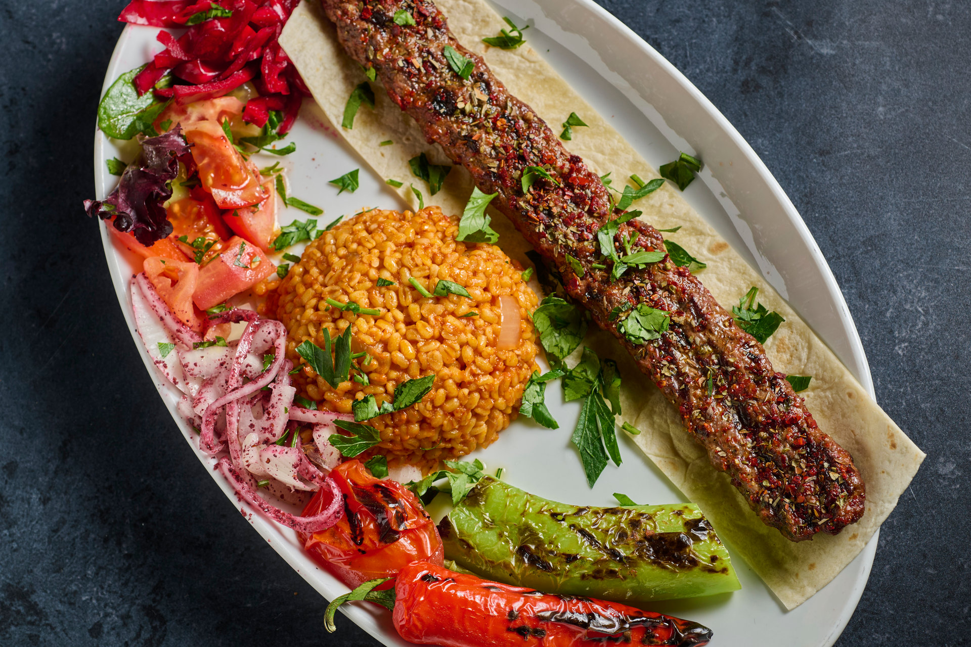 Adana kofte on flatbread with bulgur rice and grilled vegetables